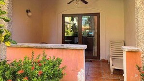Un patio al aire libre con ventilador de techo, una puerta que da a un acceso cubierto y una pequeña mesa con sillas.