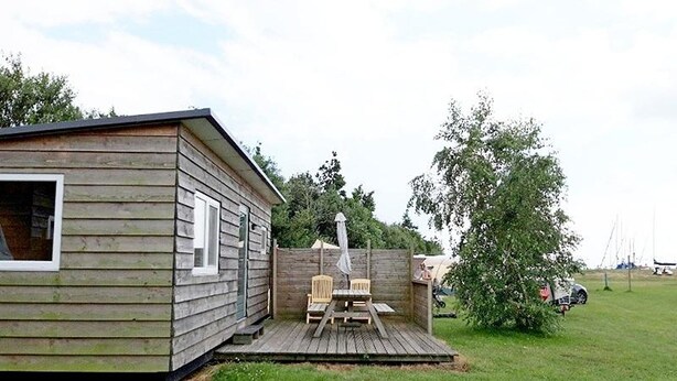 En træhytte med terrasse, to stole og et bord.