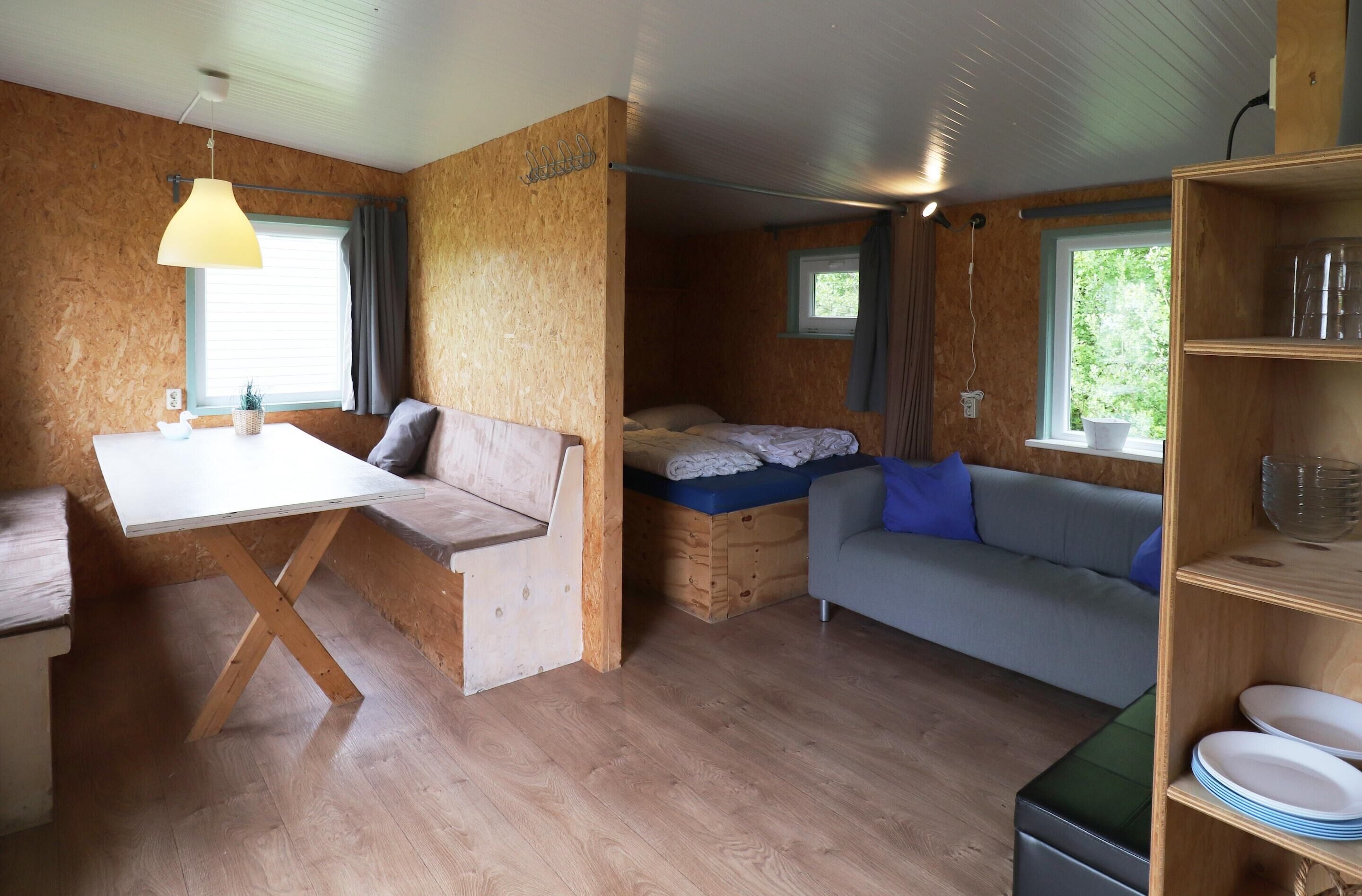Une pièce de taille modeste comprenant un lit, un canapé, une table à manger et une étagère avec de la vaisselle.