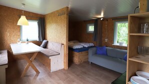 Et lille værelse med seng, sofa, spisebord og et hyldesæt med service.