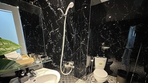 A bathroom with a black marble wall, a white sink, a toilet, and a shower. - Centana Hotel & Apartments (Ho Chi Minh City)
