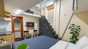 A compact hotel room with a bed, a desk with a computer, a small table with chairs, a TV, and a staircase leading to an upper level. - Centana Hotel & Apartments (Ho Chi Minh City)