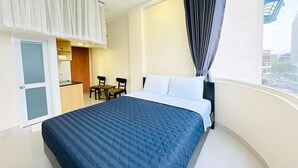 A hotel room with a bed, a small table with chairs, a kitchenette, and a large window with curtains. - Centana Hotel & Apartments (Ho Chi Minh City)