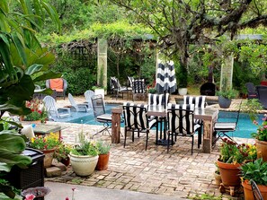 Zona junto a la piscina con sillones reclinables, una mesa y plantas en macetas.