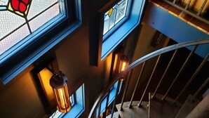 Una scala a chiocciola con ringhiere in legno e una balaustra blu, che conduce a un pianerottolo con diverse finestre.