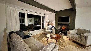 Ein modernes Wohnzimmer mit Kamin, einer Couch, einem Couchtisch und einem großen Fenster.