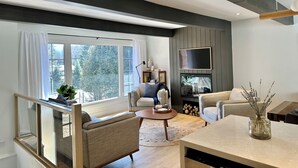 Ein modernes Wohnzimmer mit einem großen Fenster, einem Flachbildfernseher und einem Kamin.