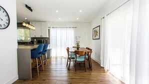 A modern kitchen with a dining area, wooden flooring, and a clock on the wall. - 3BR Palm Springs Oasis (Palm Springs)