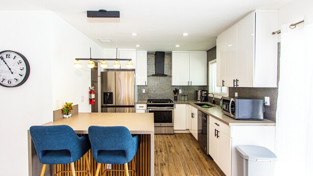 A modern kitchen with white cabinets, a wooden floor, and a dining area with two blue chairs. - 3BR Palm Springs Oasis (Palm Springs)