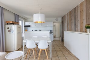 A modern kitchen with white cabinets, a dining table with four chairs, and a hanging light fixture. - One-bedroom Apartment on the Seafront (Middelkerke)