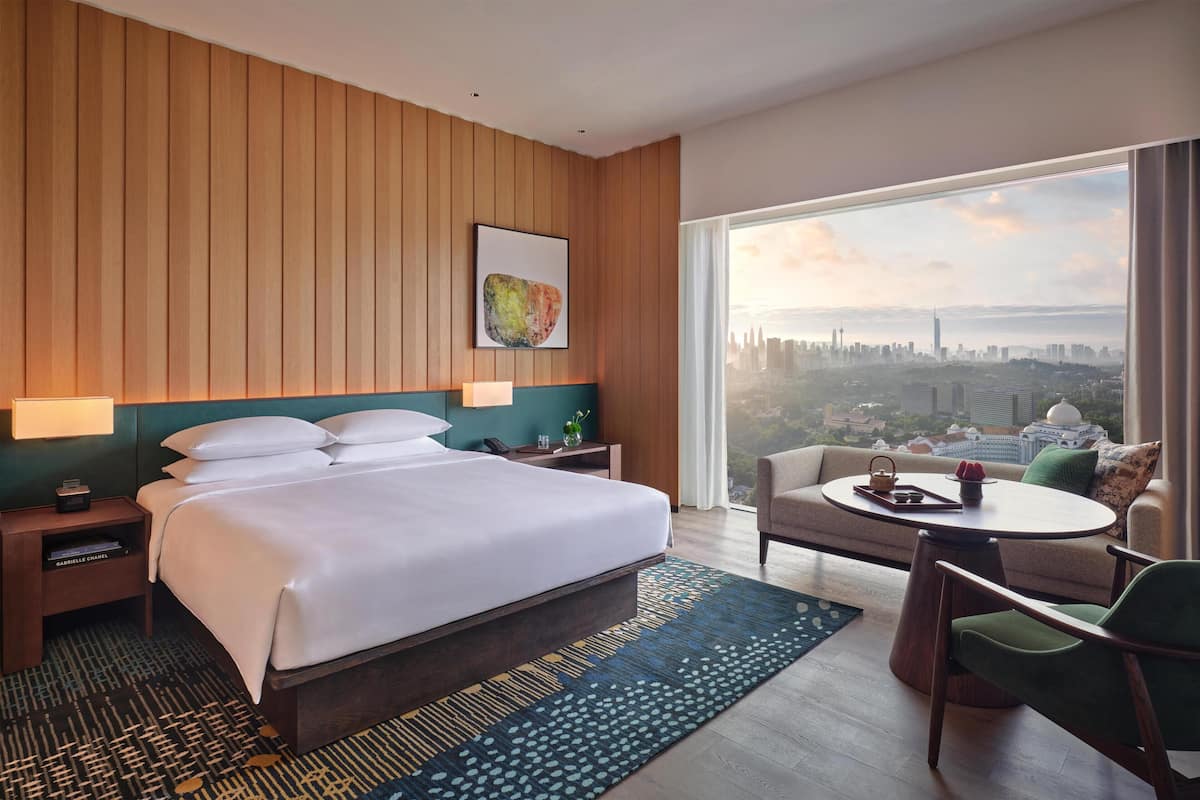 Habitación de hotel con una cama grande, zona de estar con una mesa, vistas a la ciudad y paneles de madera.