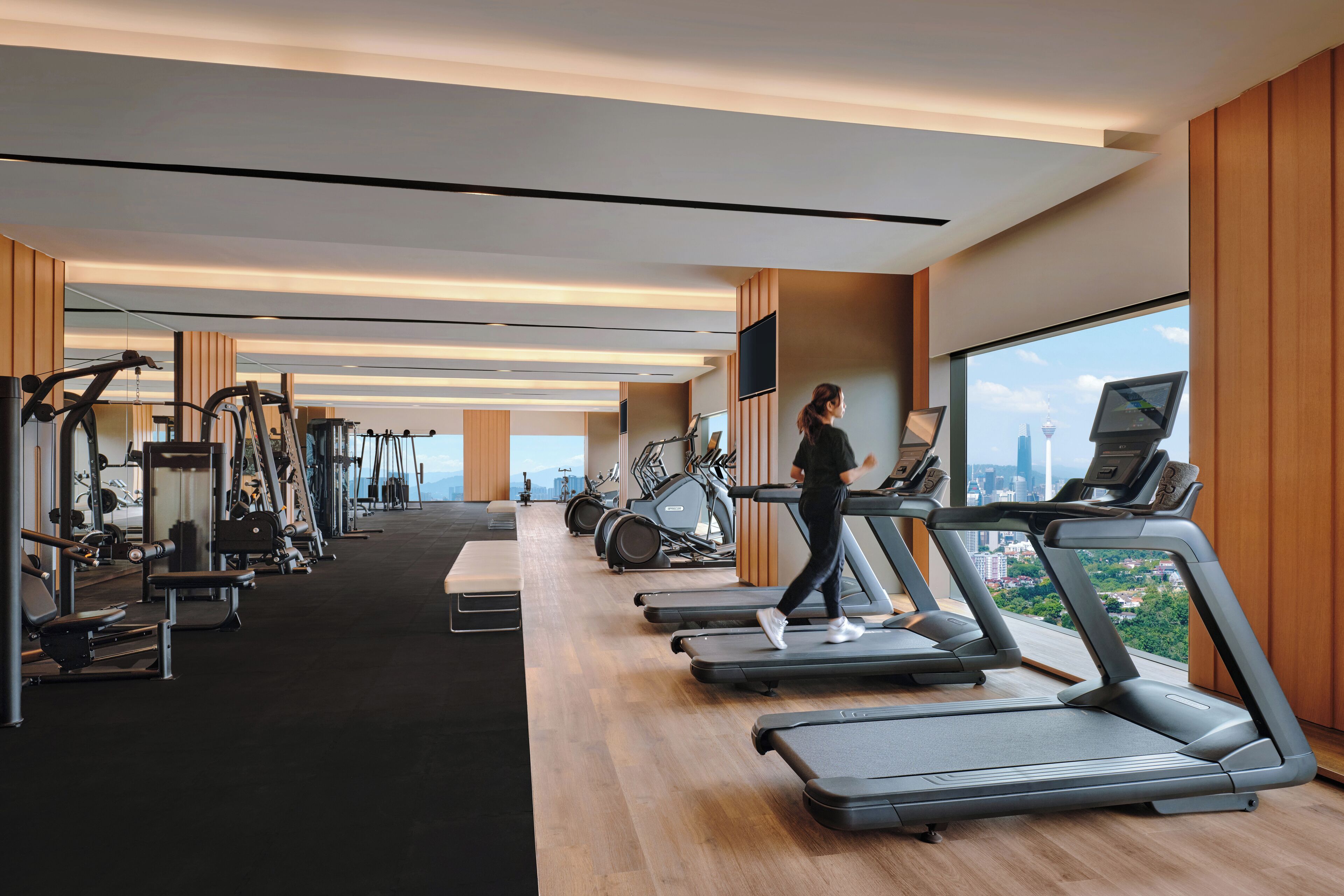 Une salle de sport moderne équipée de tapis de course, de machines de musculation et offrant une vue sur la ville.