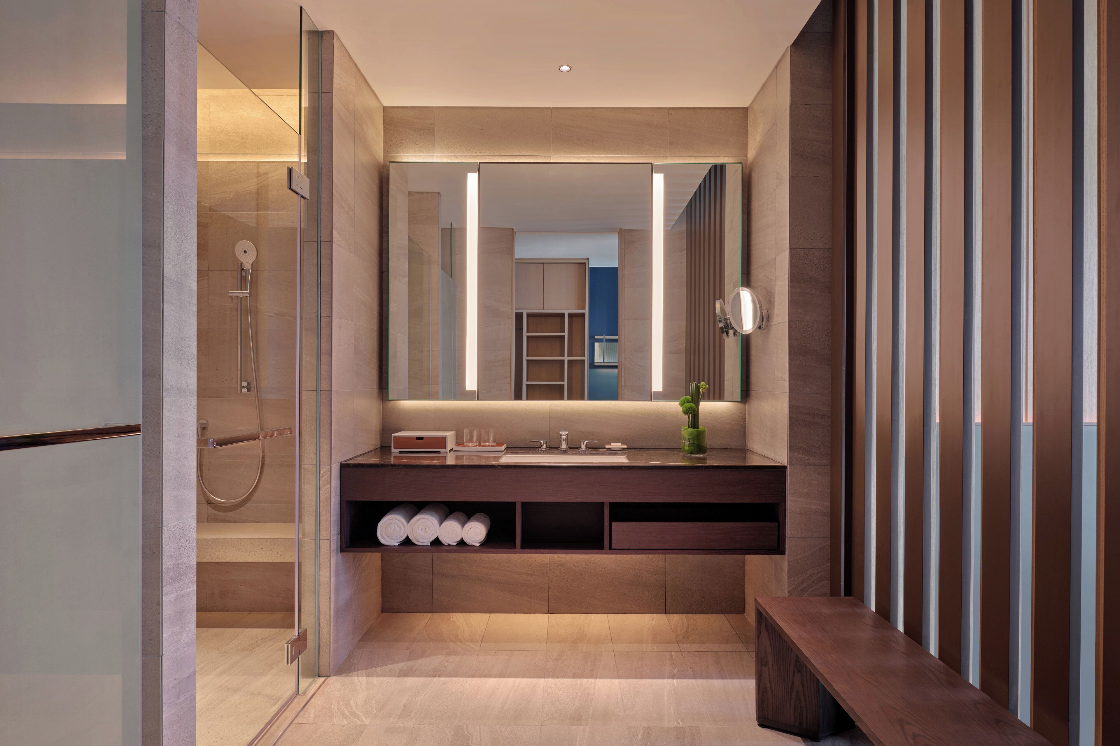 A modern bathroom with a glass-enclosed shower, a vanity with a mirror, and a bench.