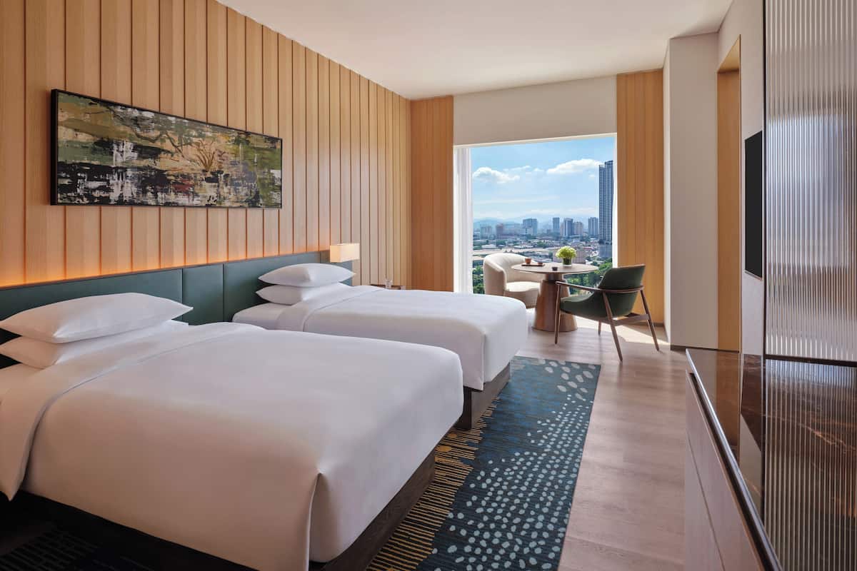 Habitación de hotel con dos camas, vista a la ciudad, zona de comedor y un televisor grande.