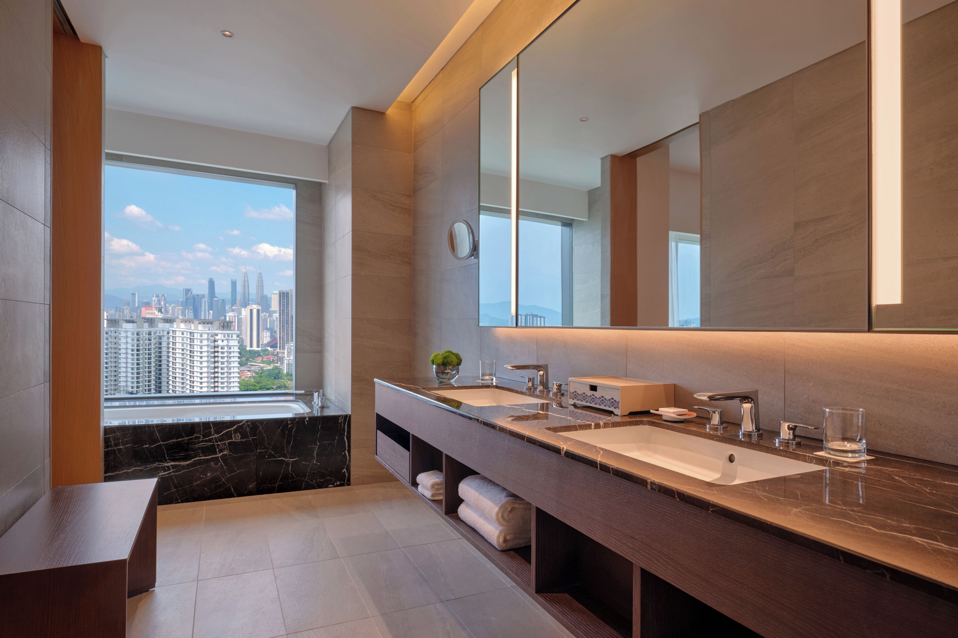 Un baño moderno con un espejo grande, lavamanos dobles, una bañera y vistas a la ciudad.