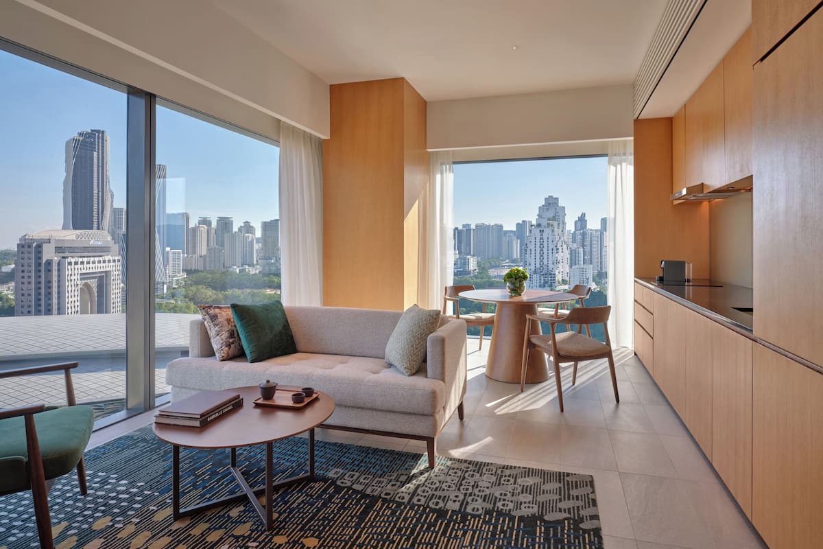 Una sala de estar moderna con sofá, mesa de centro y comedor, con ventanas amplias que ofrecen vistas a la ciudad.