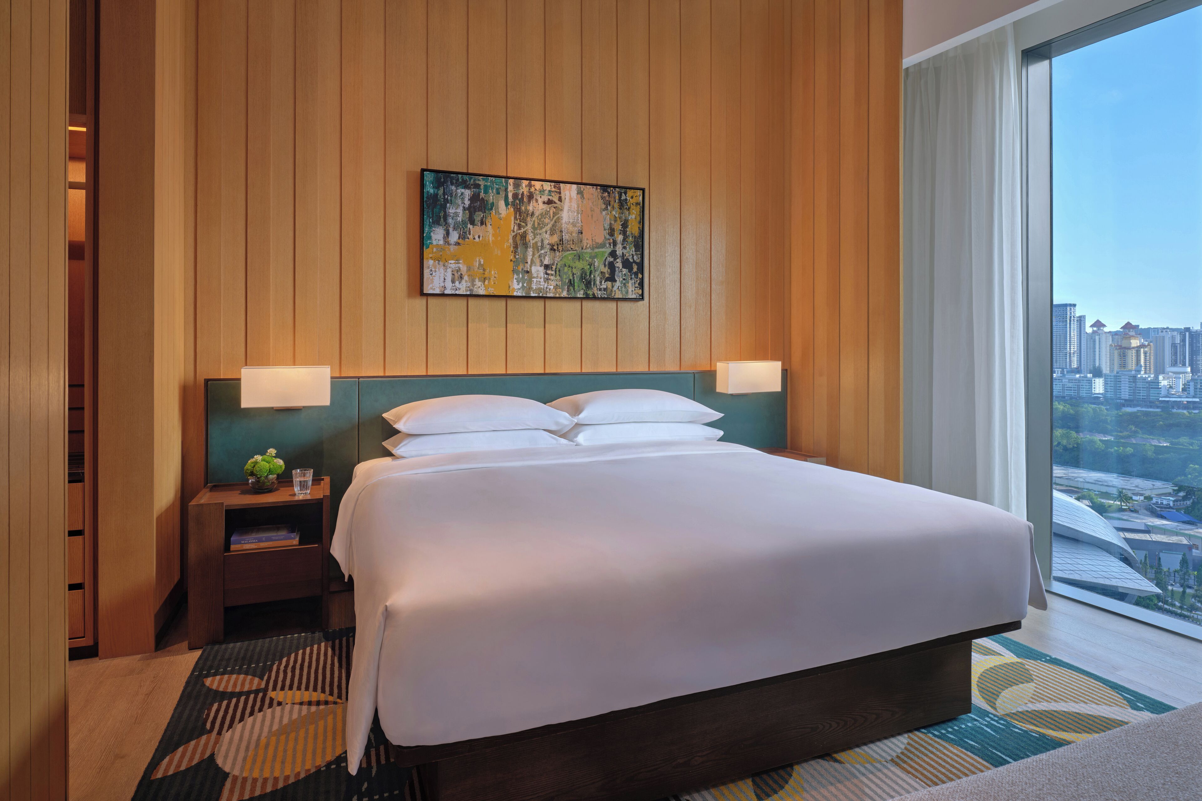 Habitación de hotel con una cama grande, paneles de madera, vista a la ciudad y un cuadro en la pared.