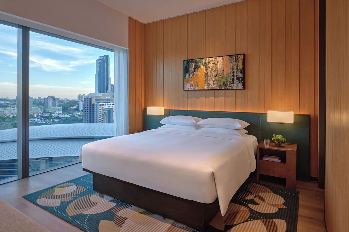 Una habitación de hotel moderna con una cama grande, vistas a la ciudad, paneles de madera y un cuadro en la pared.