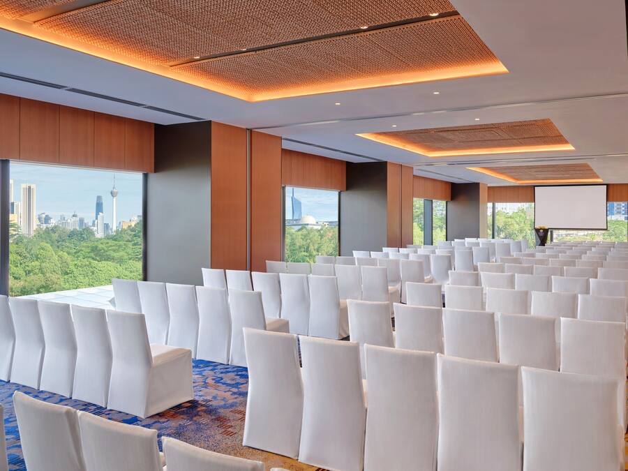 A conference room with rows of white chairs, large windows with a cityscape view, and a projector screen.