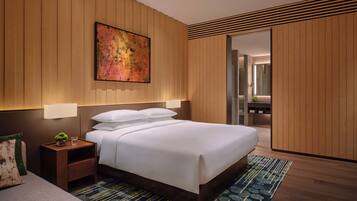 A modern hotel room with a large bed, wooden panel walls, a painting, and a nightstand with a lamp.