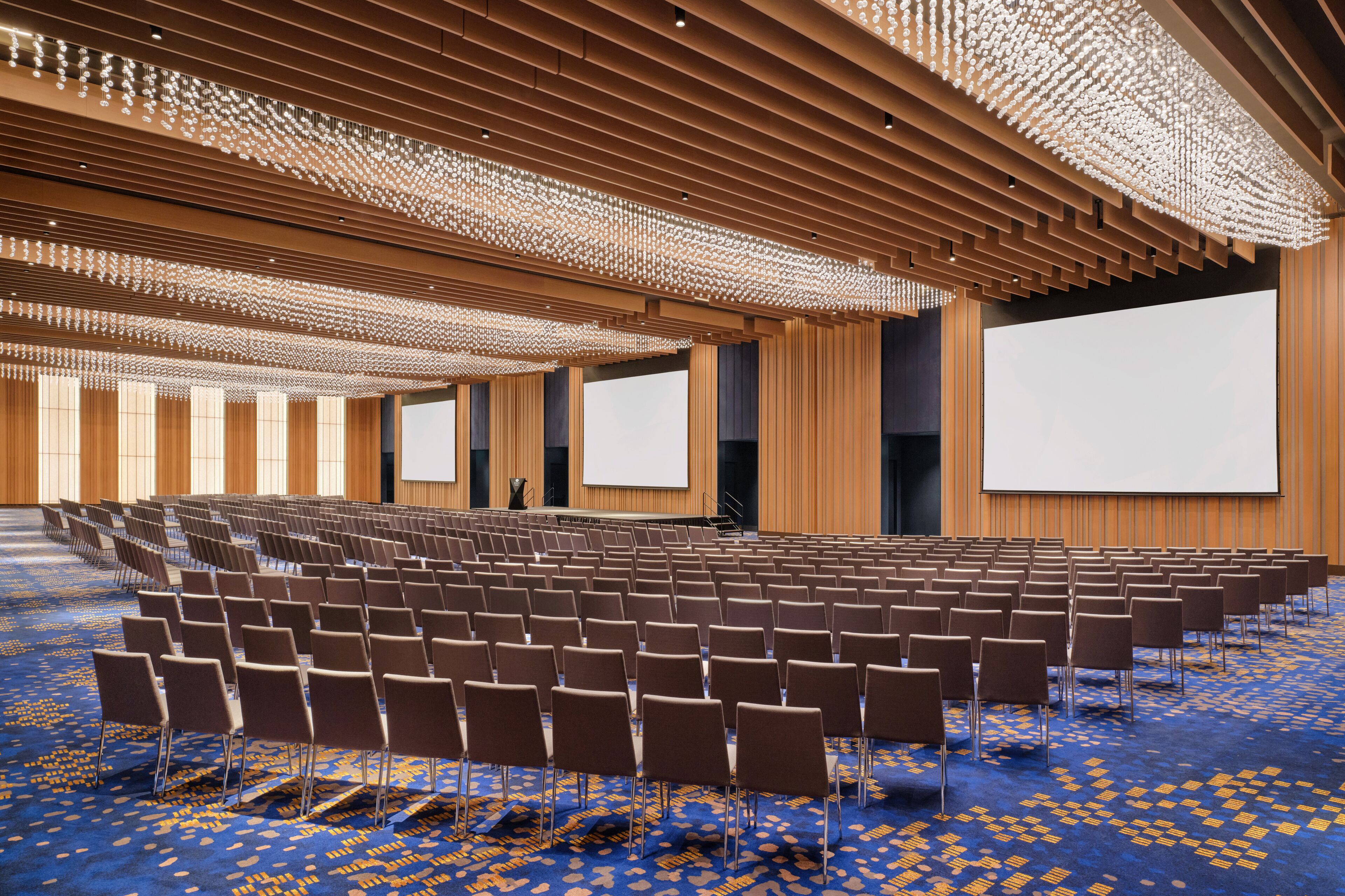 A large conference room with rows of chairs, a large screen, and a patterned carpet.