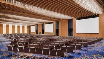 A large conference room with rows of chairs, a large screen, and a patterned carpet.