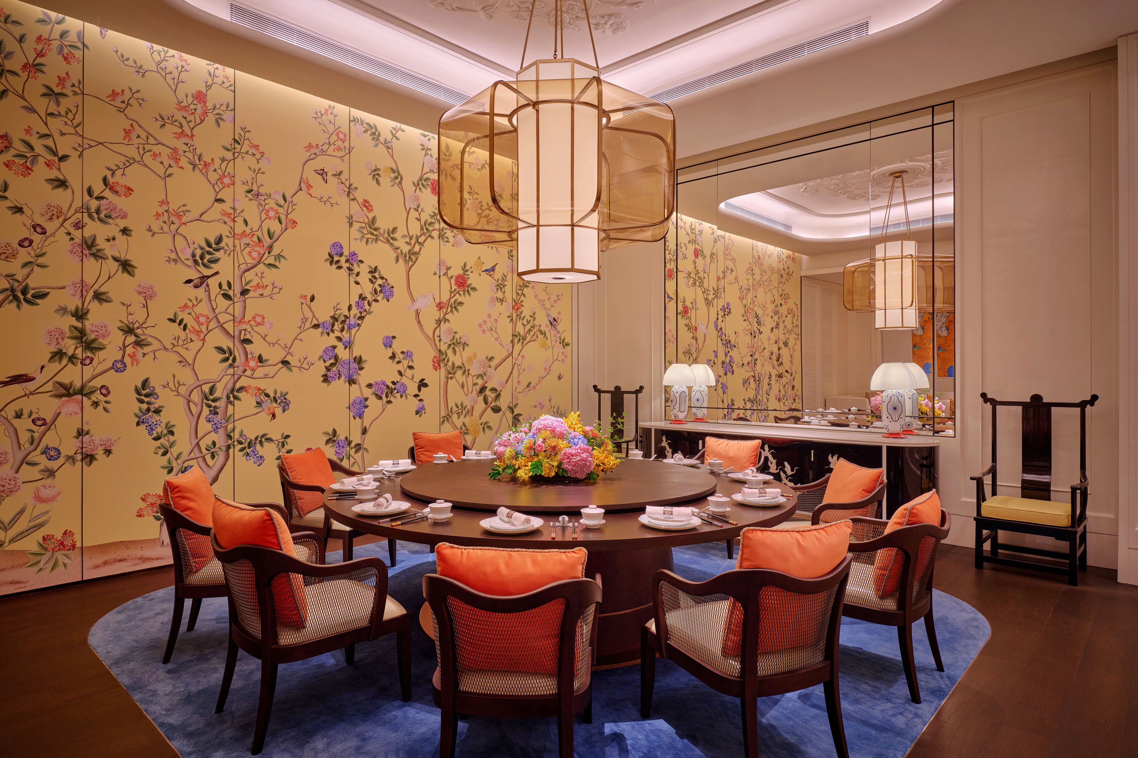 Un coin repas avec une table ronde, des coussins orange et un arrangement floral en guise de décoration centrale.