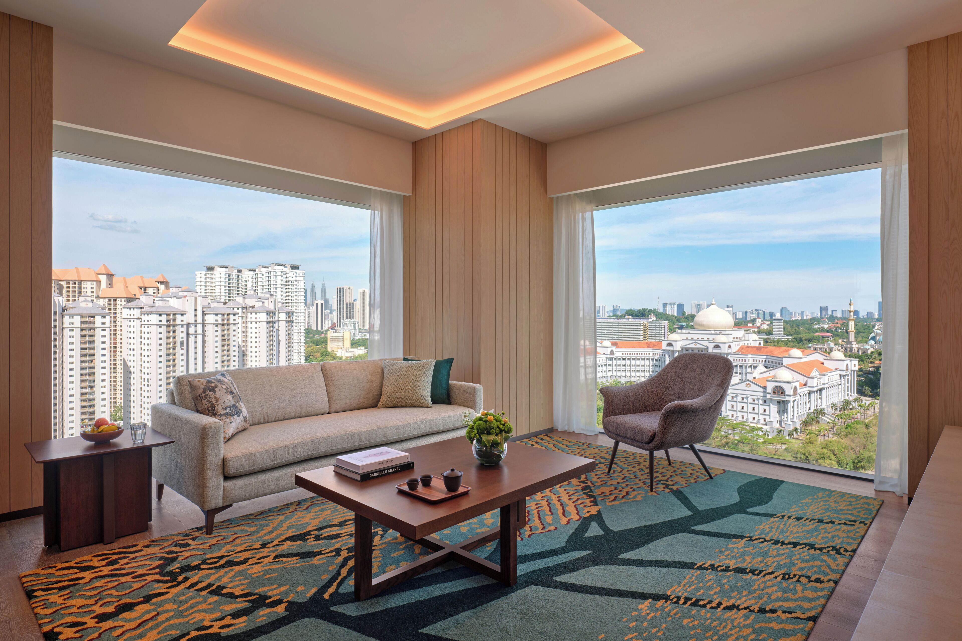 A modern living room with a sofa, armchair, coffee table, and large windows offering a city view.