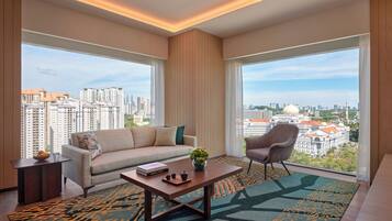 A modern living room with a sofa, armchair, coffee table, and large windows offering a city view.