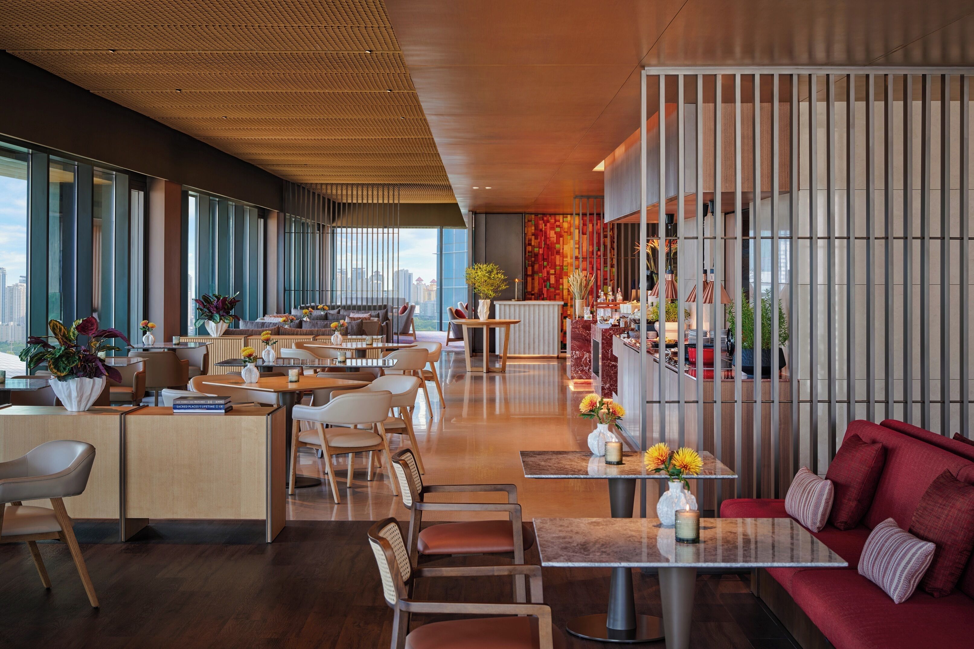 A modern hotel lobby with a mix of seating areas, including a red sofa and multiple tables.