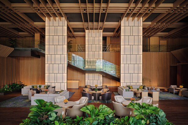 A spacious lobby with a central seating area, a staircase, and wooden paneling.