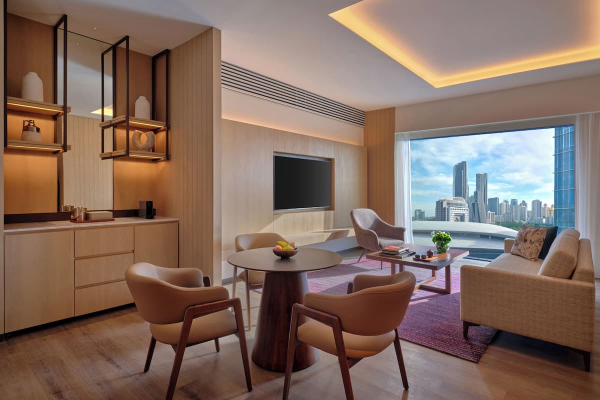Una sala de estar moderna con vistas a la ciudad, un televisor de pantalla plana y una zona de comedor con sillas y una mesa.