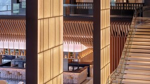 Un moderno vestíbulo de hotel con una zona de bar central, áreas de descanso y una escalera.