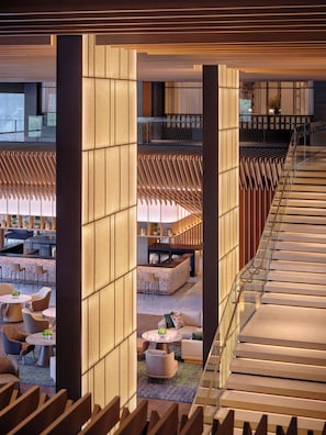 A modern hotel lobby with a central bar area, seating arrangements, and a staircase.