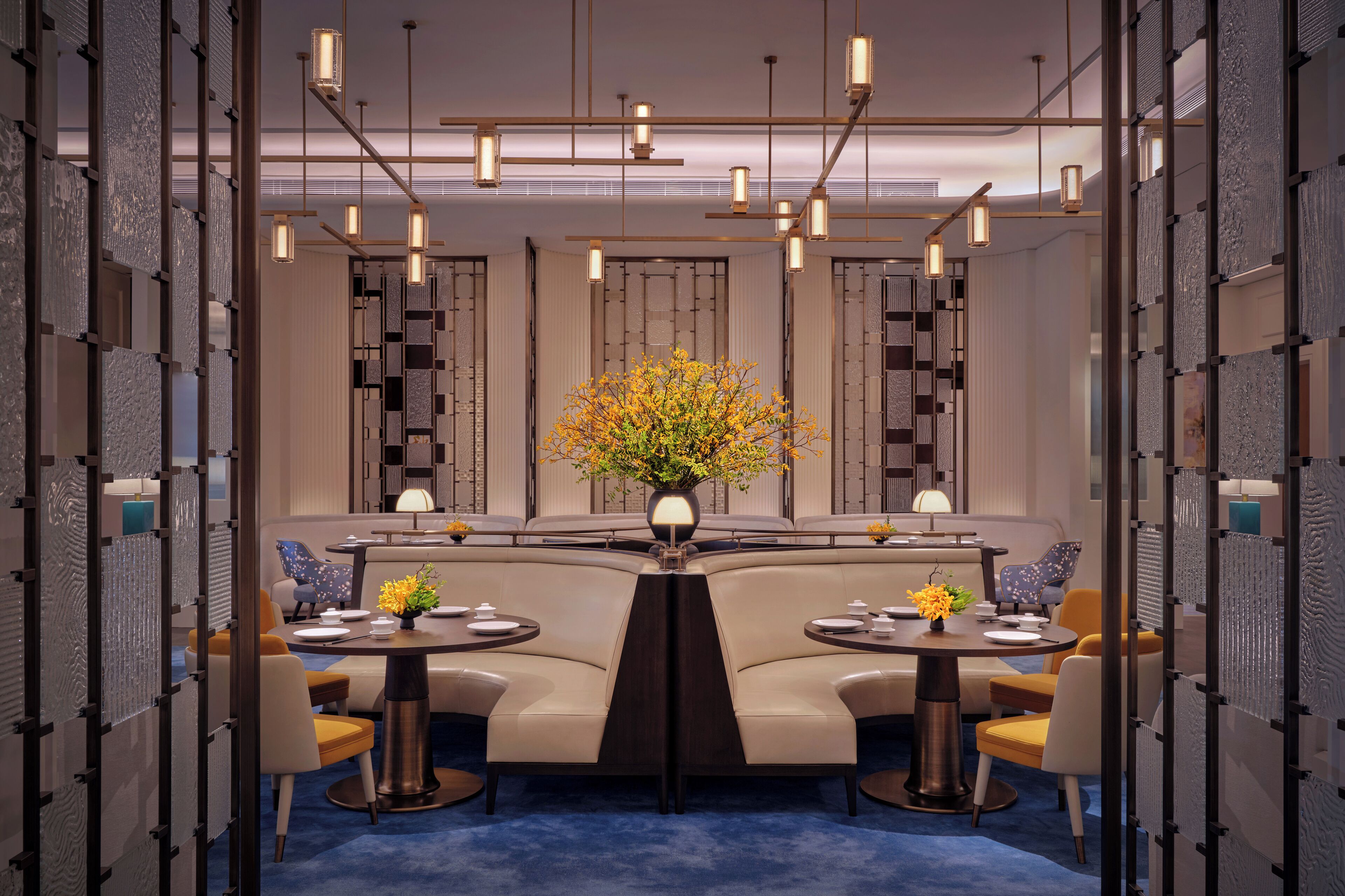A modern dining area with a central table, two sofas, and a decorative vase of flowers.