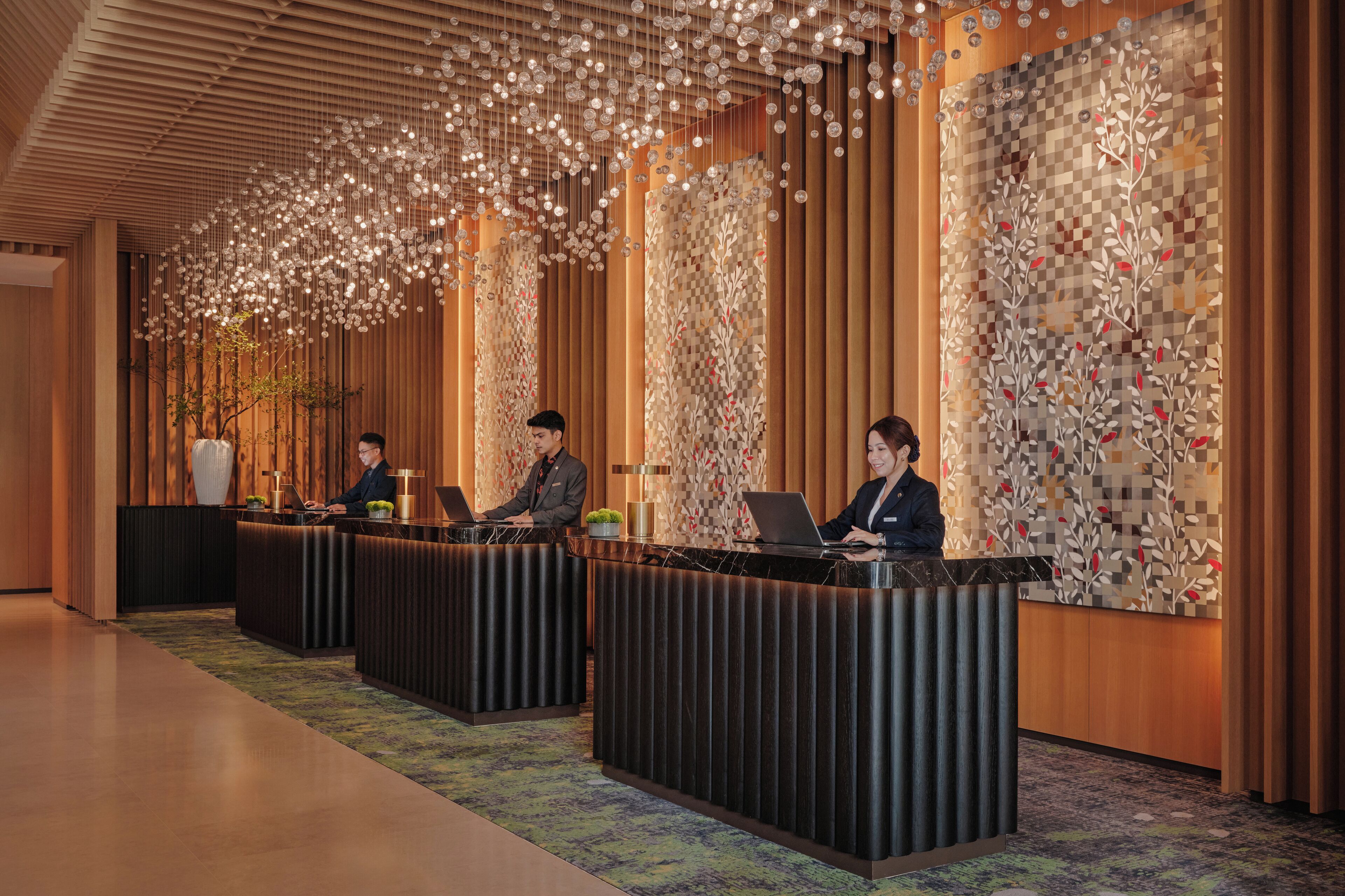 A reception area with three receptionists at their desks, wooden paneling, and a decorative ceiling.