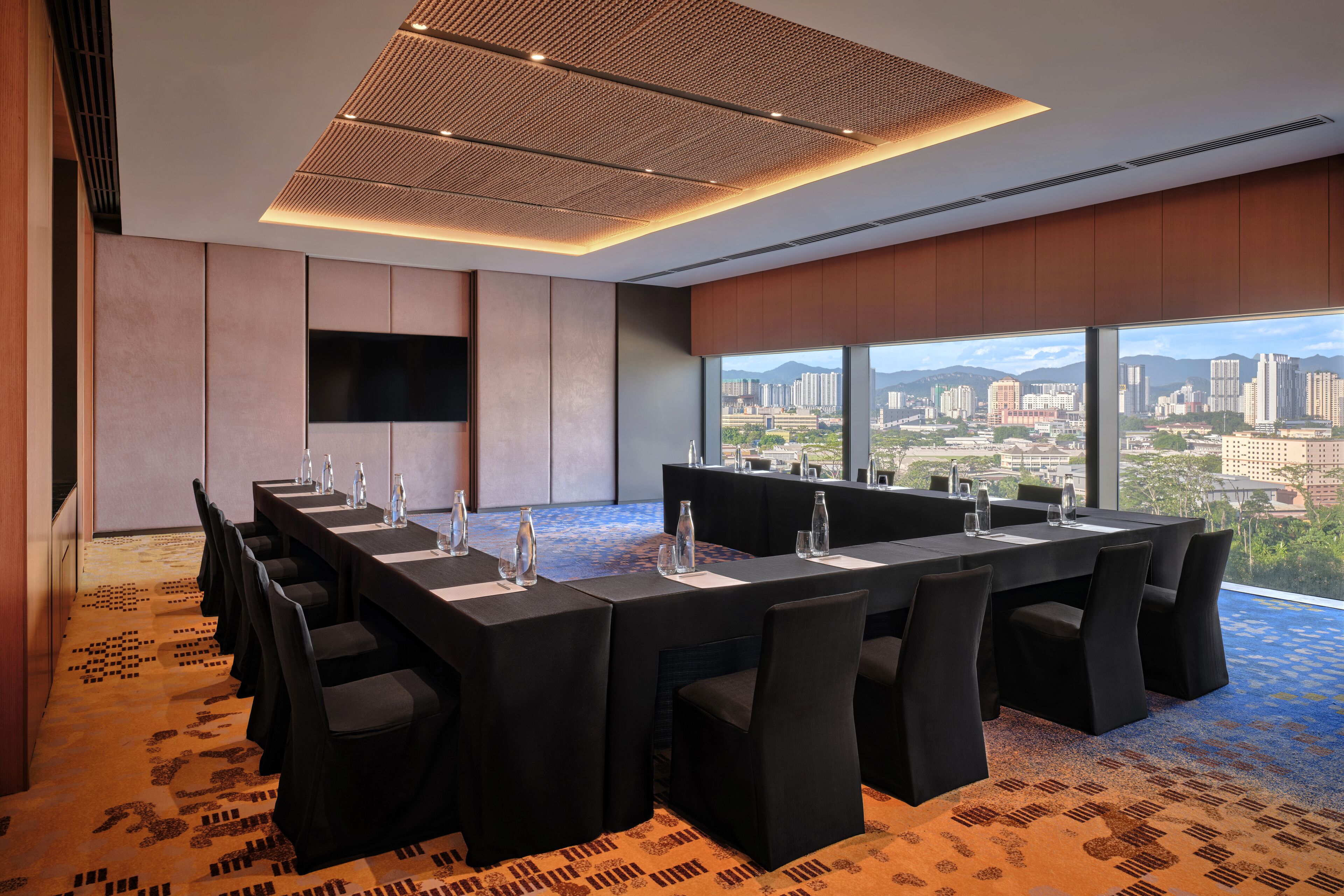 A conference room with a city view, equipped with a large table, chairs, and a flat-screen TV.