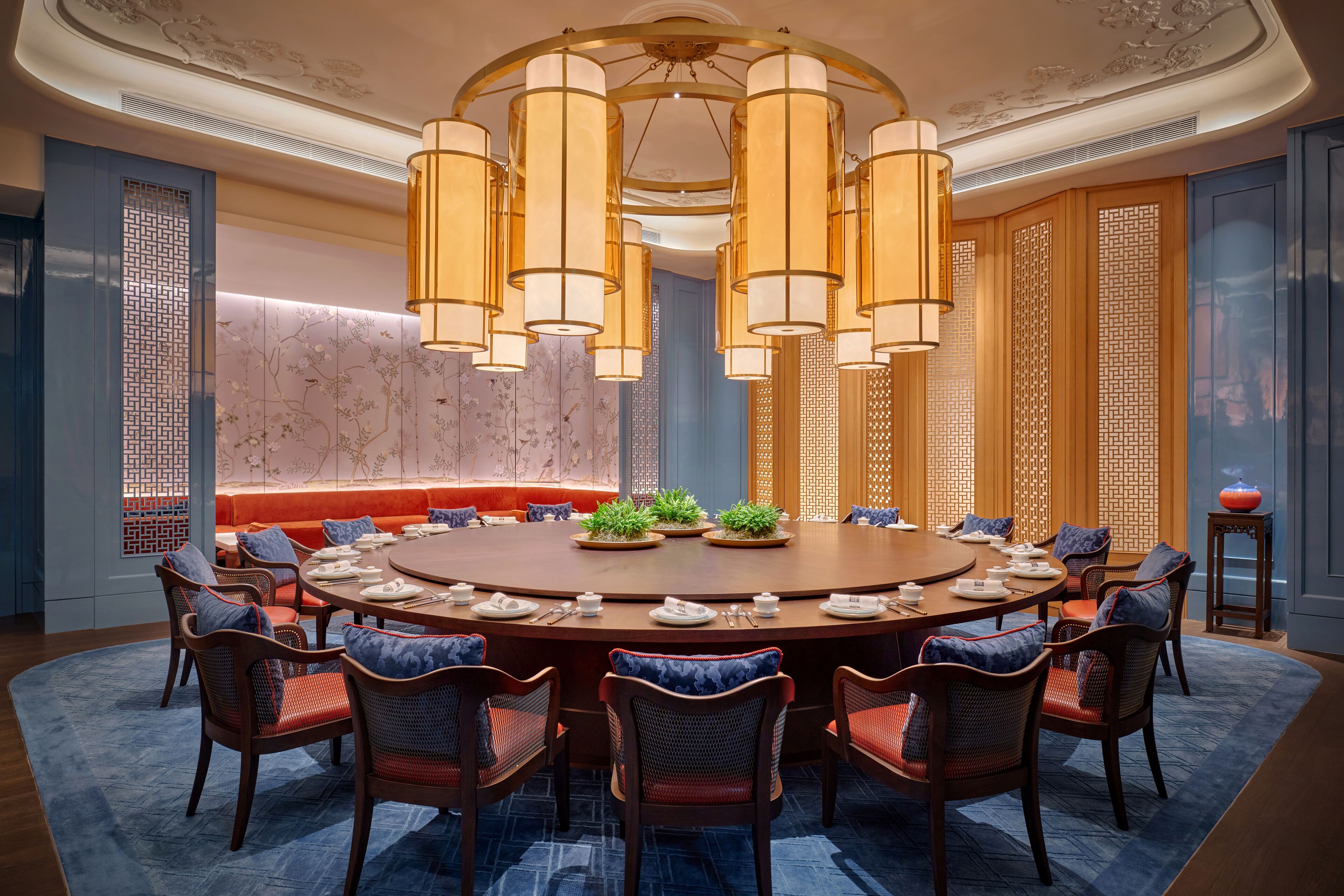 A round dining table with eight chairs, a chandelier, and a blue patterned rug.
