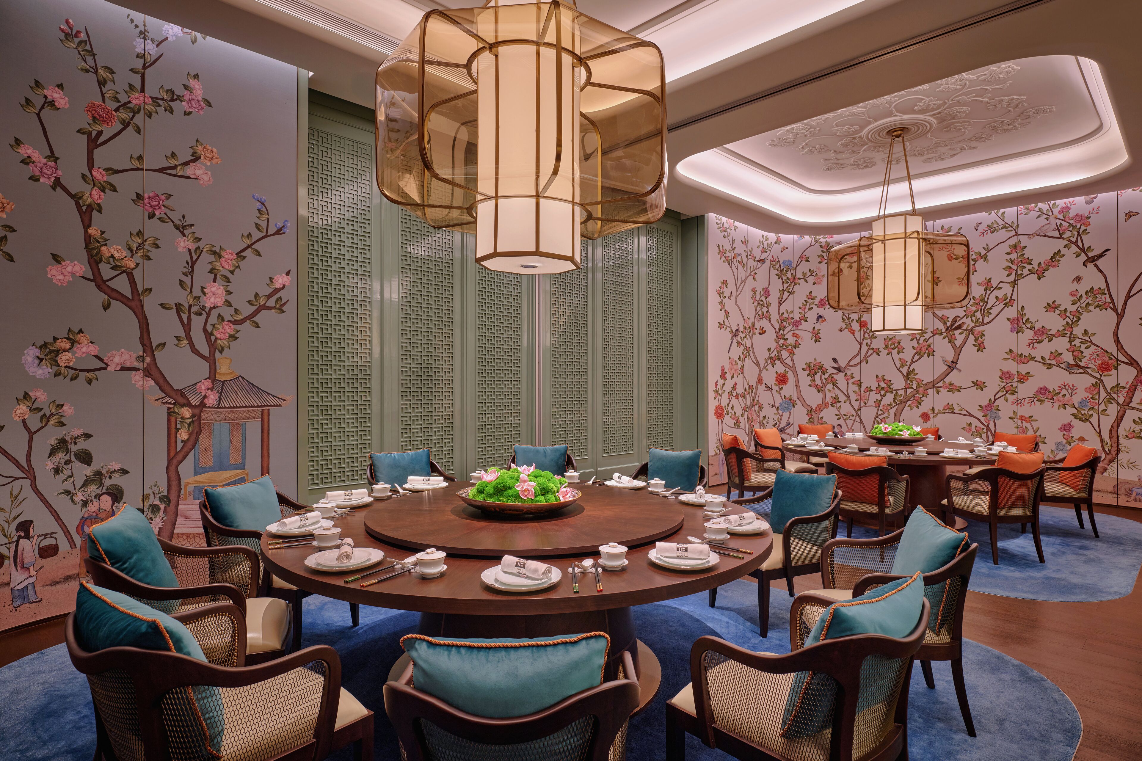A round dining table with chairs, surrounded by floral wall art and traditional Chinese lattice panels.
