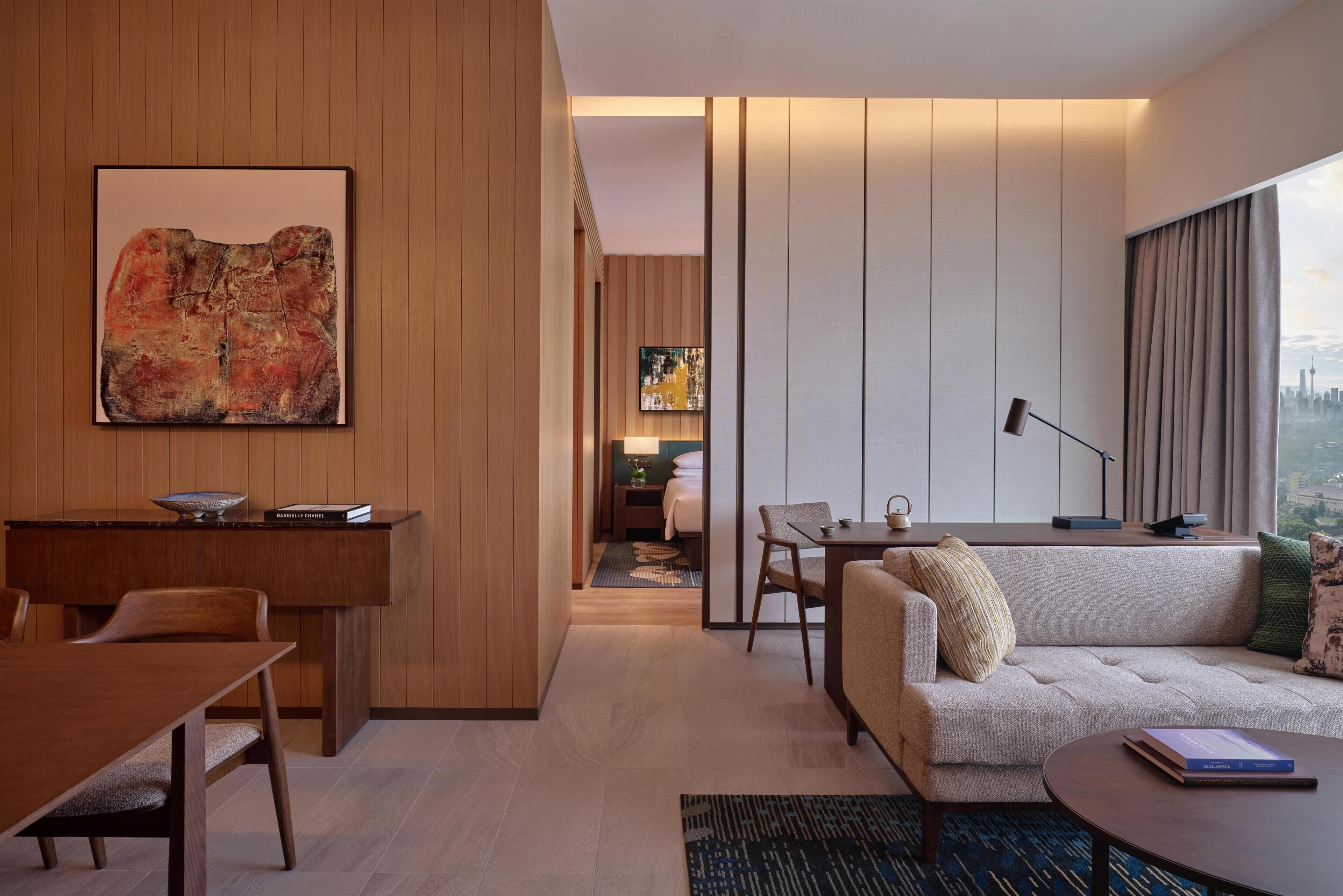 Une chambre d’hôtel moderne comprenant un coin repas, un canapé, une table basse et un grand tableau abstrait accroché au mur.