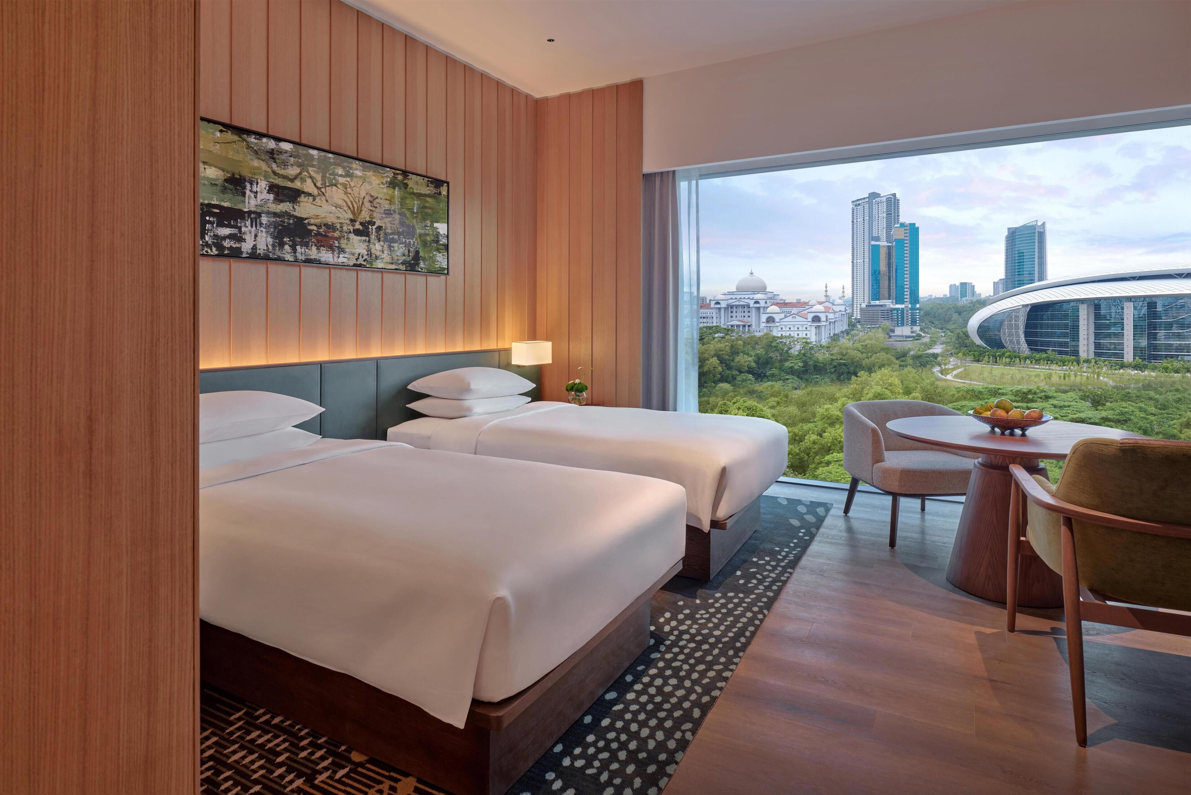 A hotel room with two beds, a dining table, and a view of a cityscape.