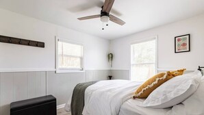 Une chambre à coucher comprenant un lit, un banc, un ventilateur de plafond et deux fenêtres.