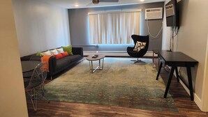 A modern living room with a dark sofa, a black chair, a coffee table, and a TV mounted on the wall. - Downtown Suite Living! (Minneapolis)