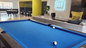 A pool table in a modern indoor space with a neon sign, seating area, and visible windows. - Downtown Suite Living! (Minneapolis)