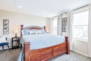 Een slaapkamer met een houten bed, een nachtkastje, een stoel en een raam met gordijnen.