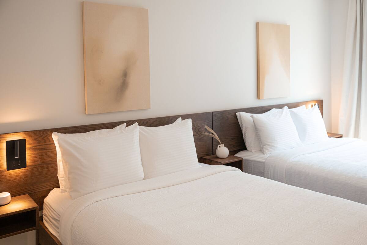 A hotel room with two beds, wooden headboards, white bedding, and wall-mounted artwork.