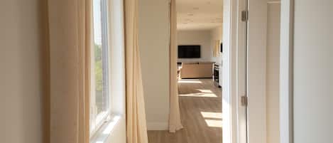 Un couloir avec un plancher en bois, des rideaux beiges et un tĂ©lĂ©viseur Ă lâarriĂšre-plan.