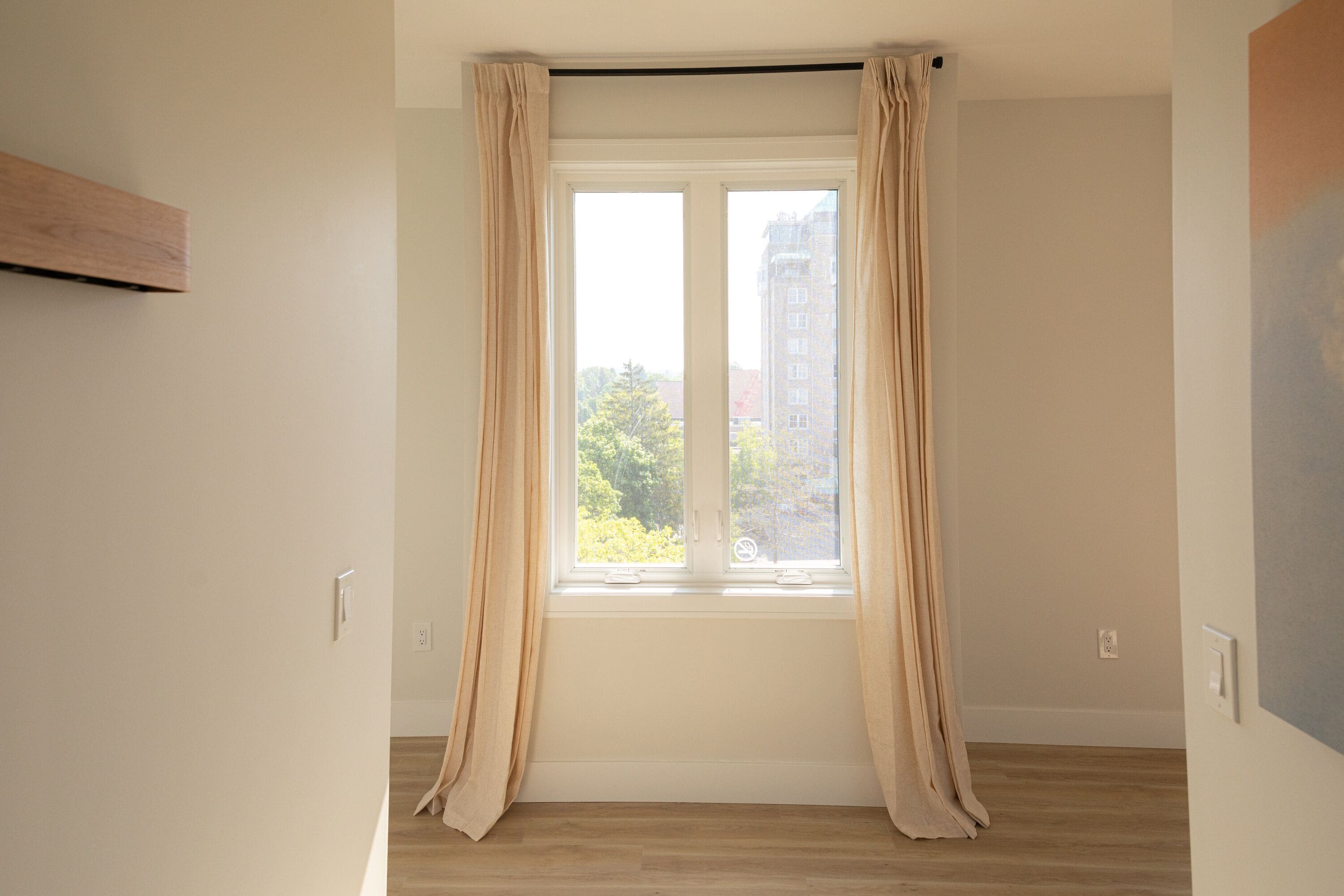 A room with a large window, wooden flooring, and a plain wall.
