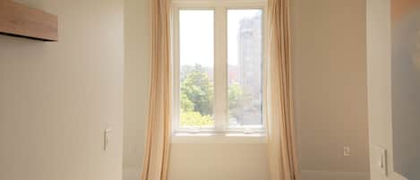 A room with a large window, wooden flooring, and a plain wall.