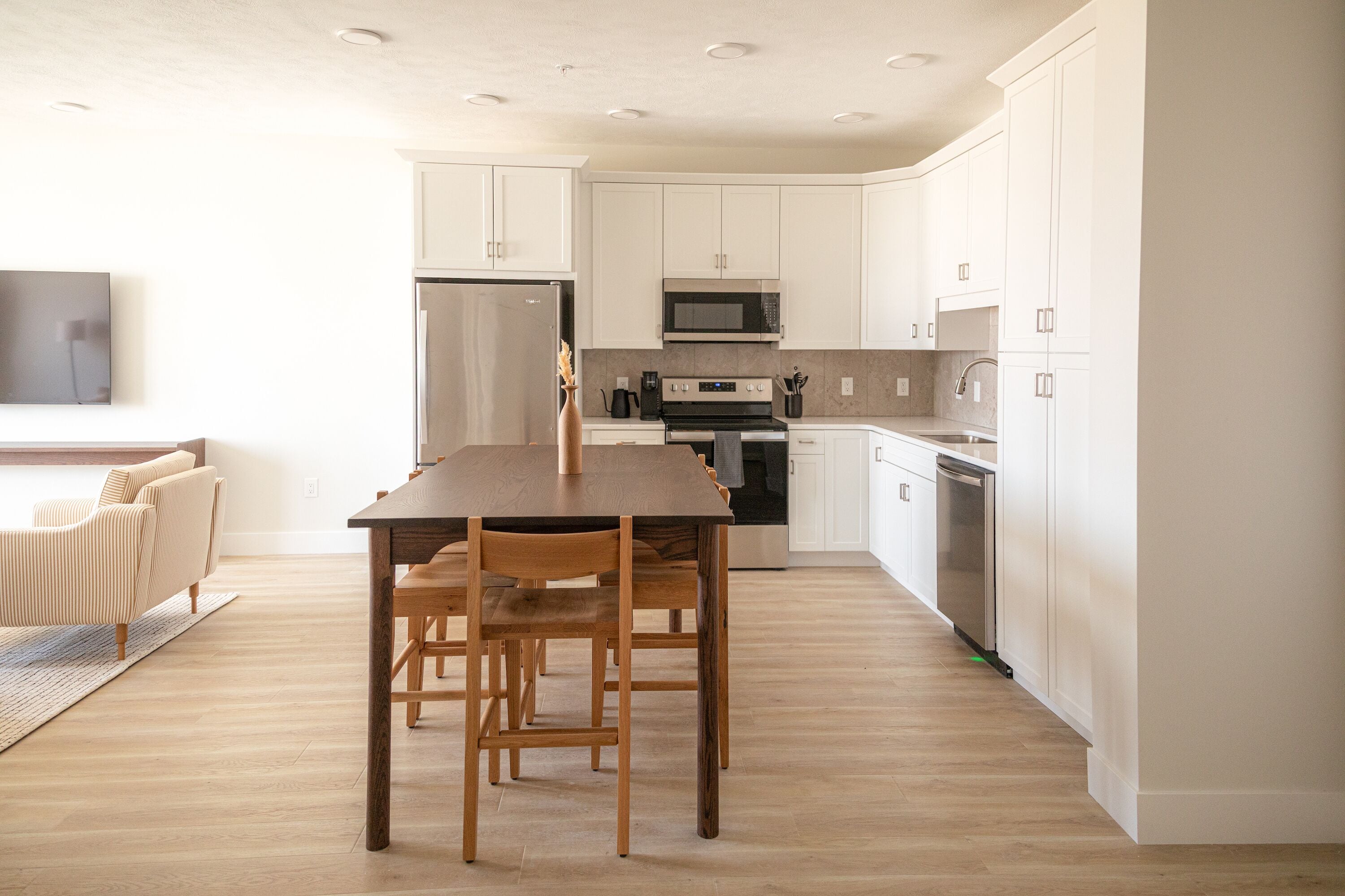 Una cocina moderna con armarios blancos, una mesa de comedor de madera y un horno empotrado.